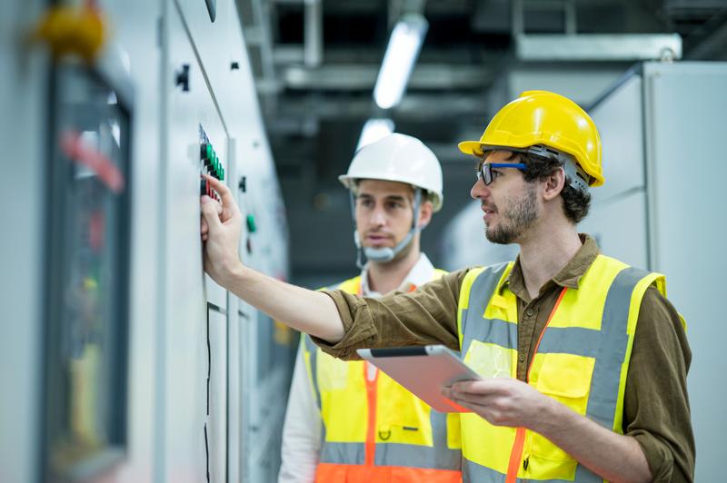 Elektrotechniker im Industrieservice stehen nebeneinander und tauschen sich vor einer Schalttafel aus. Konzept des Energiemanagementsystems (EMS).