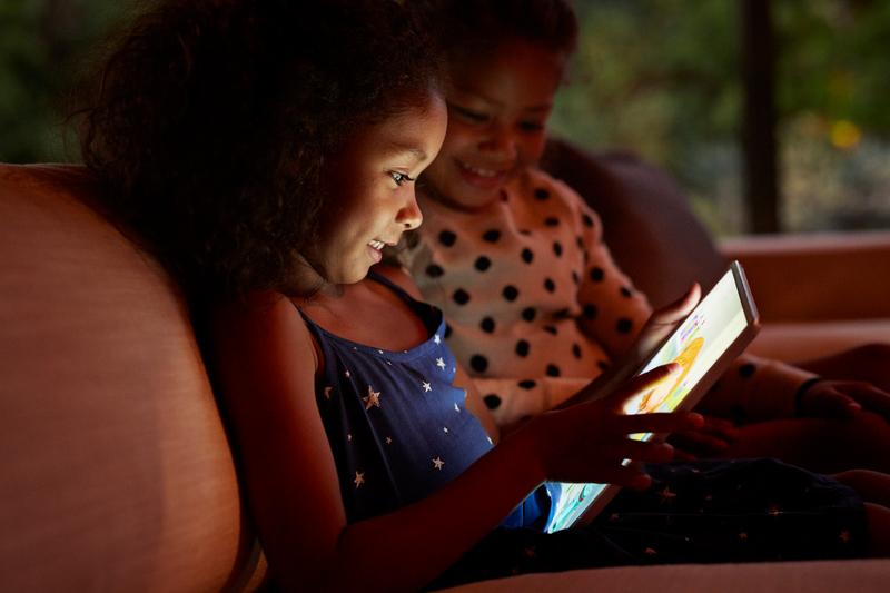 Two young girls playing on digital tablet%2C at night