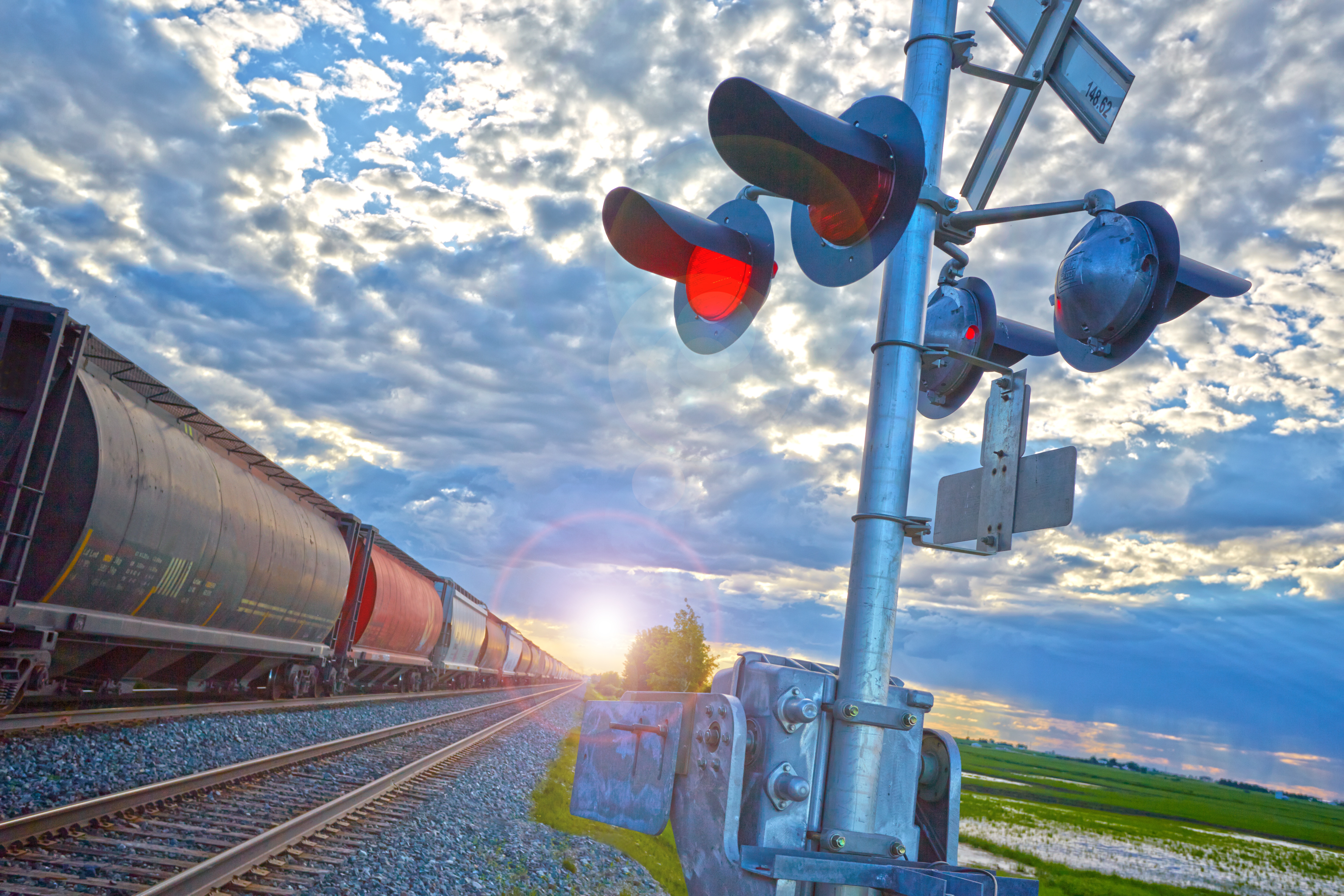 Freight train moving through remote urban crossing in late afternoon against sunny sky. 