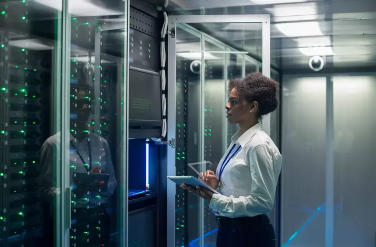 Medium shot of female technician working on a tablet in a data center full of rack servers running diagnostics and maintenance on the system