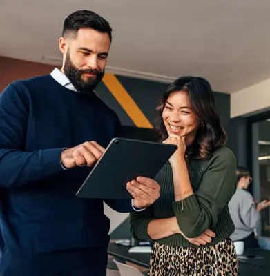 Happy business colleagues using a digital tablet in a boardroom. Two young businesspeople having a discussion during a meeting. Diverse entrepreneurs working together as a team.