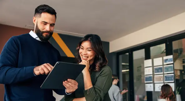 happy business colleagues using a digital tablet in a boardroom. two young businesspeople having a discussion during a meeting. diverse entrepreneurs working together as a team.