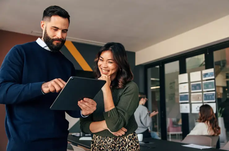 happy business colleagues using a digital tablet in a boardroom. two young businesspeople having a discussion during a meeting. diverse entrepreneurs working together as a team.