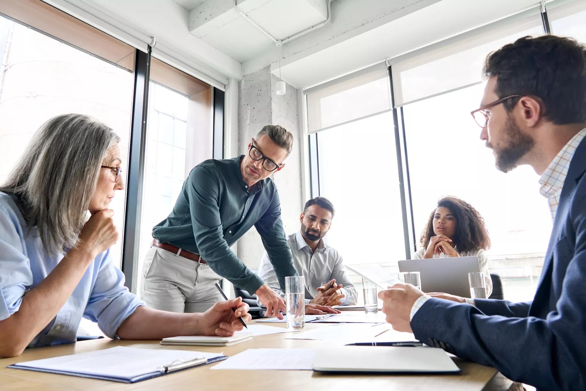 male mature caucasian ceo businessman leader with diverse coworkers team, executive managers group at meeting. multicultural professional businesspeople working together on research plan in boardroom.