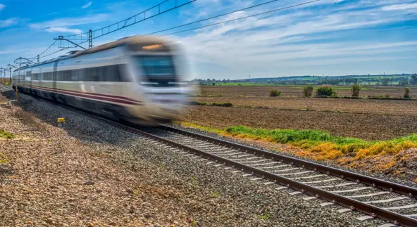 Un train à grande vitesse, flou en mouvement, traverse un paysage rural sous un ciel d'un bleu éclatant.