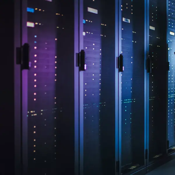 In Dark Data Center: Male IT Specialist Stands Beside the Row of Operational Server Racks, Uses Laptop for Maintenance. Concept for Cloud Computing, Artificial Intelligence, Supercomputer. Neon Lights
