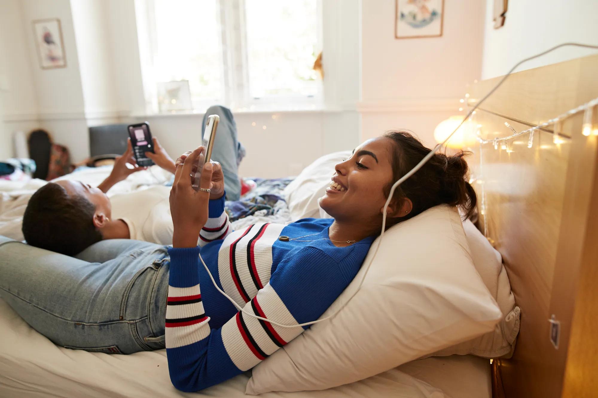 Smiling woman using mobile phone with friend on bed