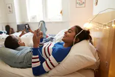 smiling woman using mobile phone with friend on bed