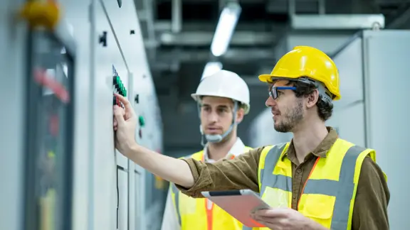 industrial service electrician engineers standing side by side having exchange idea in front of electricity control board. energy management system (ems) concept.