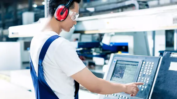 worker entering data in cnc machine at factory floor to get the production going