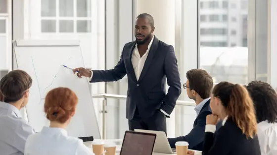 African american conference speaker coach talk to audience give presentation on flipchart to employees group, black trainer manager speaking training diverse corporate team at office meeting seminar