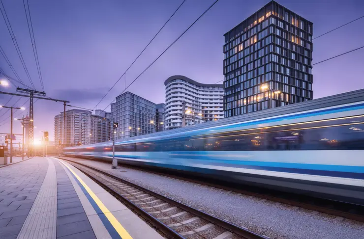 High speed train in motion on the railway station at sunset. Moving blue modern intercity passenger train, railway platform, buildings, city lights. Railroad in Vienna, Austria. Railway transportation