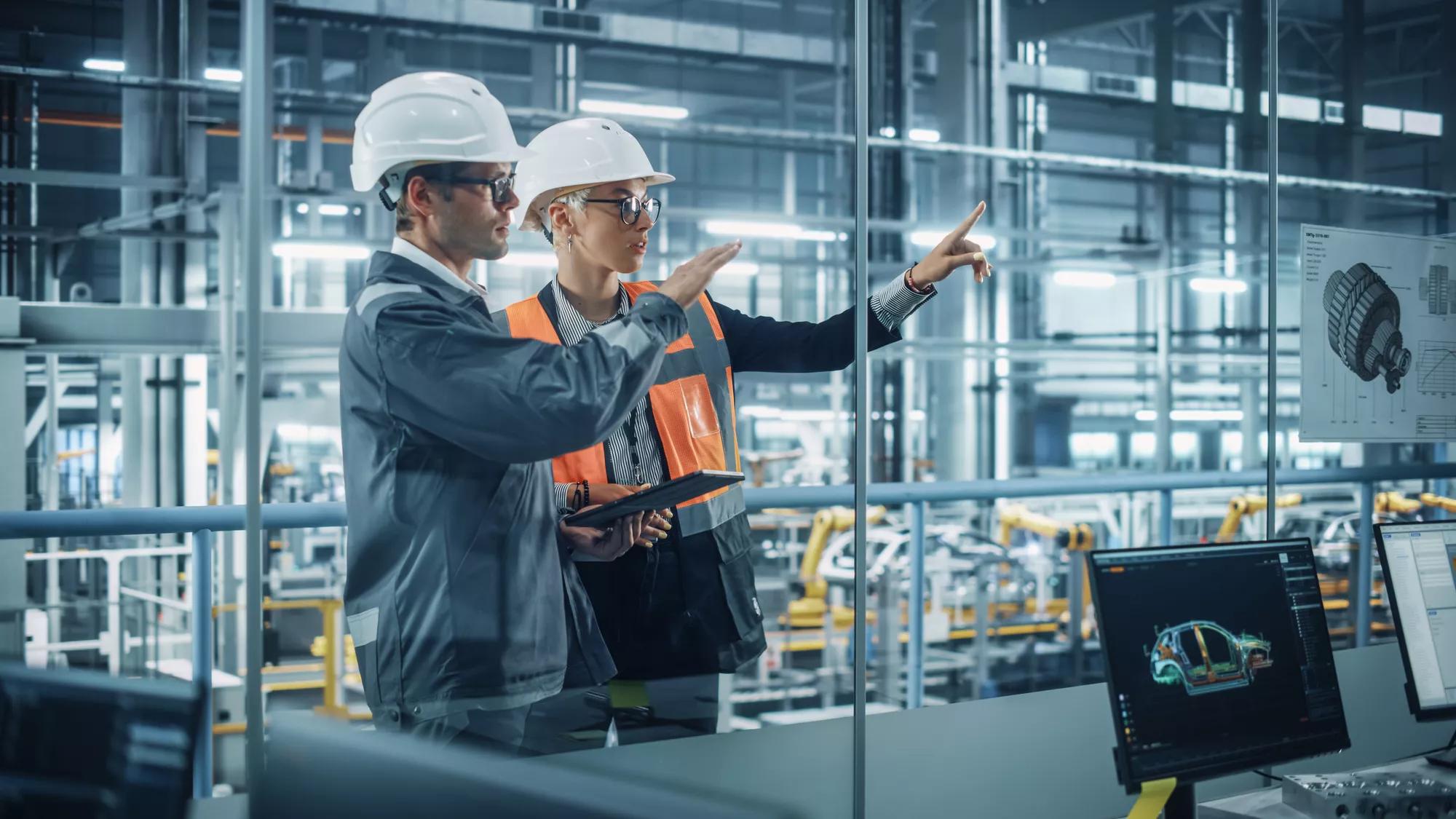 Male Engineer and Female Industrial Product Designer Discuss Work while Using Tablet in Office at a Car Assembly Plant. Industrial Specialists Working on Vehicle Design in Technological Factory.