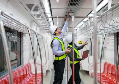 Deux mécaniciens travaillant ensemble dans la fosse d'inspection d'un centre de maintenance ferroviaire, se concentrant sur la réparation des trains et les mesures de sécurité, illustrent le travail d'équipe essentiel et les enjeux industriels.