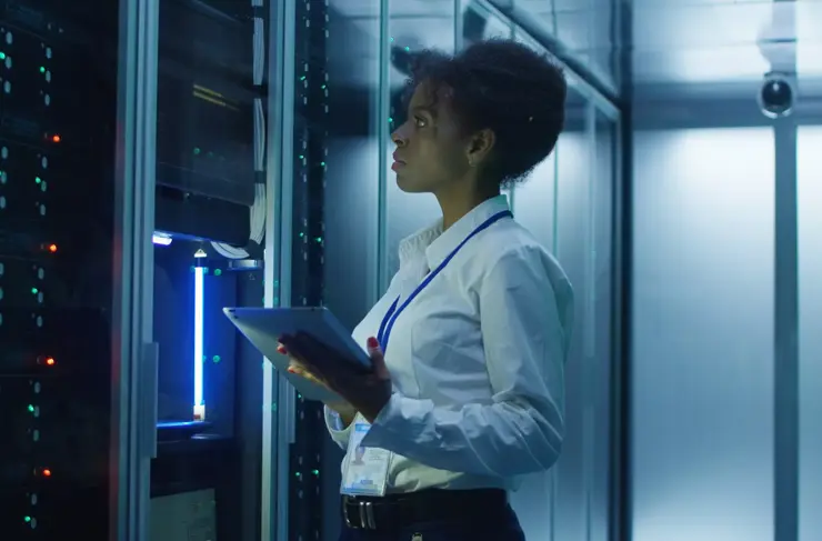 Formal African American woman using tablet while working with server rack in contemporary data center hallway