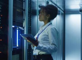 Formal African American woman using tablet while working with server rack in contemporary data center hallway