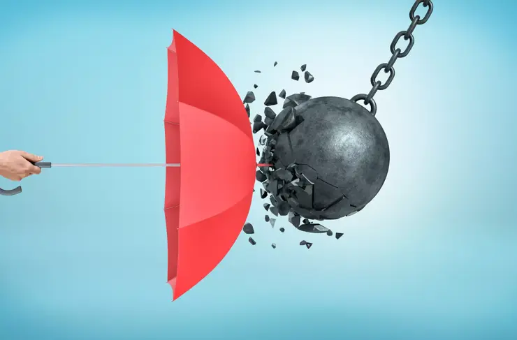 A male hand holding an open red umbrella which protects from a collision with a broken wrecking ball. Insurance and protection. Safety measures. IT defense.