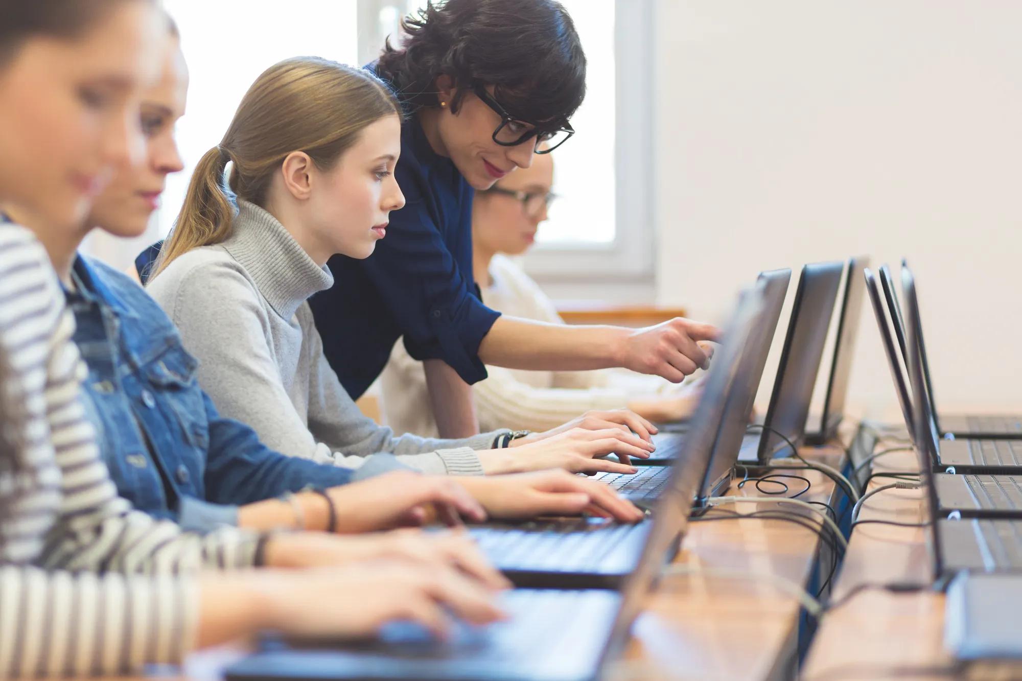 Female students learning computer programming with teacher