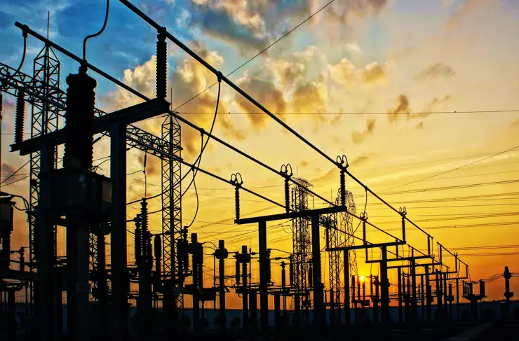 Image d'un réseau aérien de transformateurs haute tension sur poteaux au lever du soleil, sur un fond de ciel avec tonalité jaune, cadre horizontal 