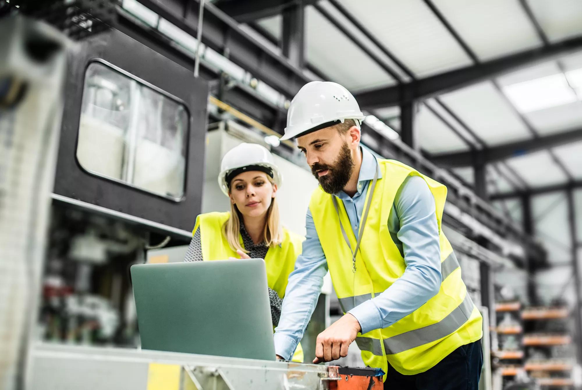 Industrial engineers conferring on operational plans with PC on manufacturing floor.