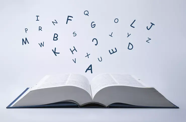 English dictionary with letters flying out of it on a white background.