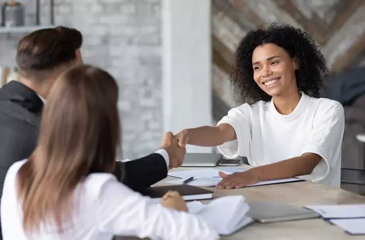 smiling african american businesswoman shaking business partner hand at corporate meeting, greeting and acquaintance, making agreement, great commercial deal, sitting at table in boardroom