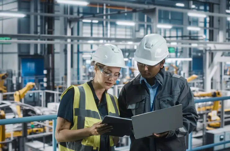 male specialist and female car factory engineer talking and working on laptop and tablet computers. automotive industry 4.0 facility working on vehicle production. diversity on assembly plant.