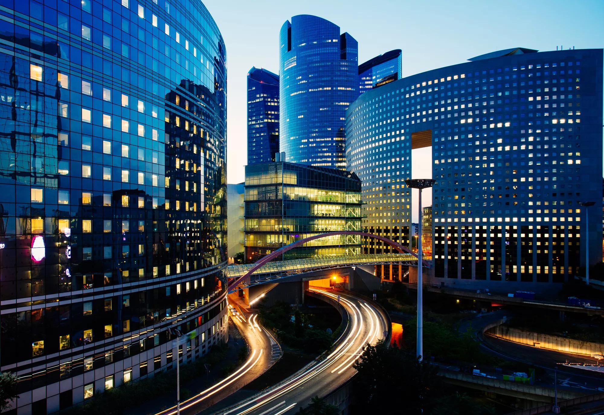 Night architecture - skyscrapers with glass facade. Modern buildings in Paris business district. Evening dynamic traffic on a street. Concept of economics, finances.  Copy space for text. Toned