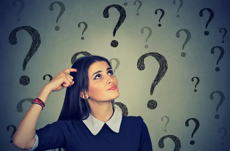 Portrait confused thinking young woman bewildered scratching head seeks a solution looking up at many question marks isolated on gray wall background. Human face expression