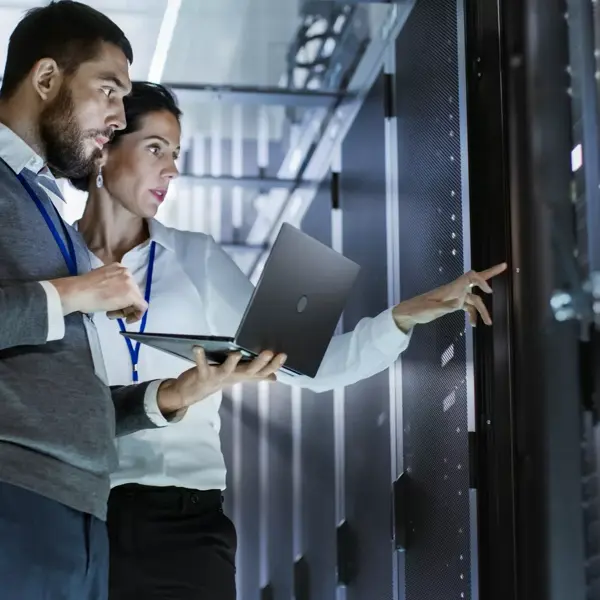Male & female data center technicians, one with laptop, troubleshoot in front of server cabinet