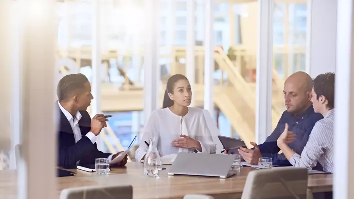 Gruppe von vier Unternehmern mit dynamischer Erfahrung und vielseitigem Hintergrund, die alle damit beschäftigt sind, zusammenzuarbeiten und während eines geplanten wöchentlichen Treffens miteinander zu sprechen.