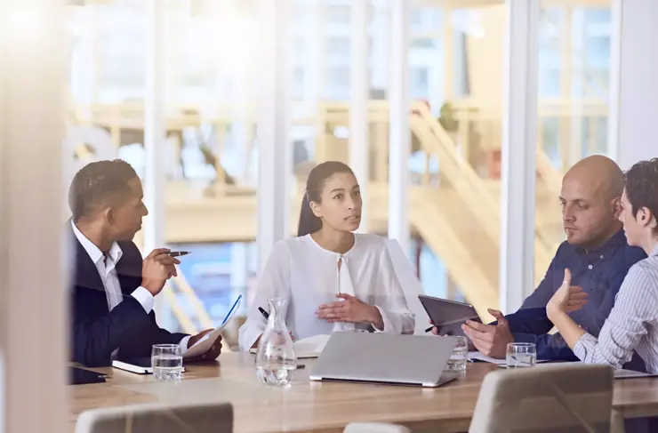Group of four entrepreneurs with dynamic experience and eclectic backgrounds, all busy working together and talking to one and other during a scheduled weekly meeting.