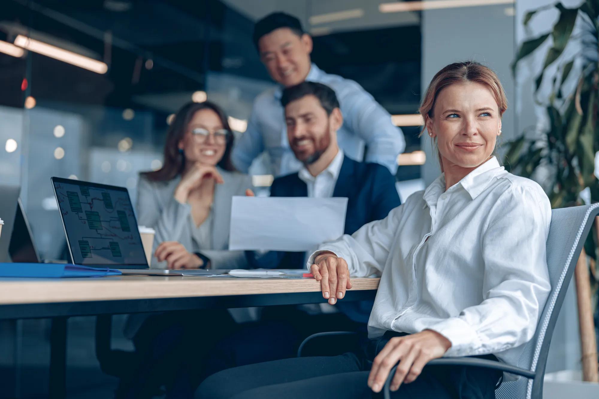 Reflective confident businesswoman sitting on meeting in office with her colleagues at background