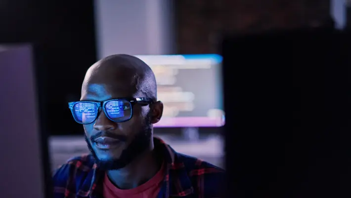Cyber security, black man and code reflection in eyewear, hacking and software update in office. African American male employee, programmer or IT specialist with glasses, focus and cloud computing